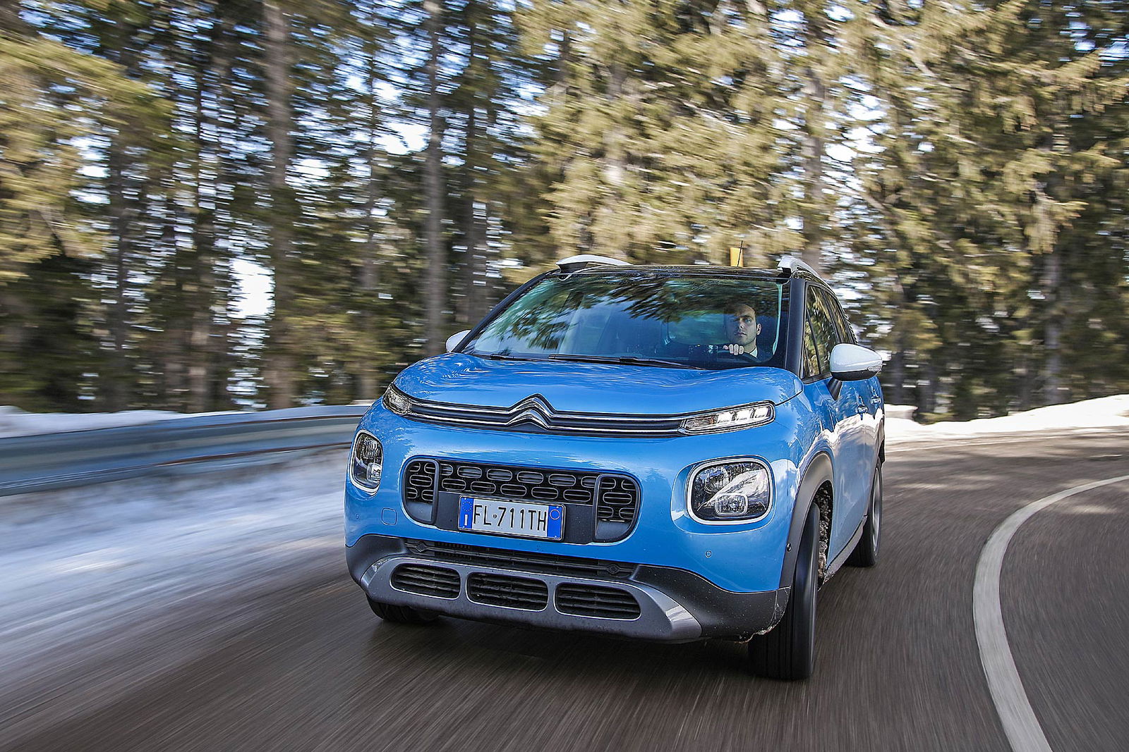 Citroën C3 Aircross azzurra impegnata in curva asfaltata di montagna tra pini e neve