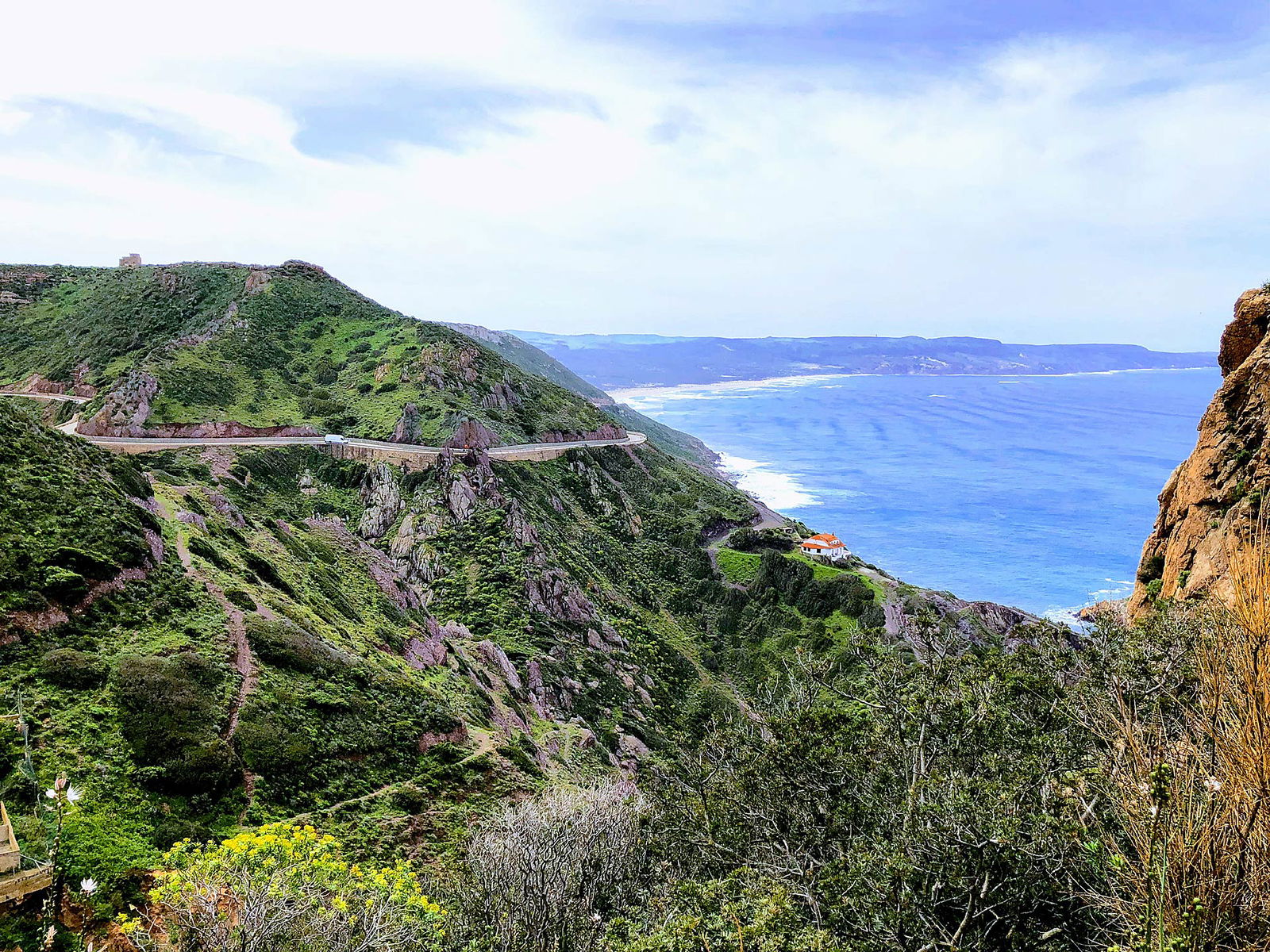 Vista dall'alto di una strada tortuosa della Sardegna del Sud, sullo sfondo si scorge il mare