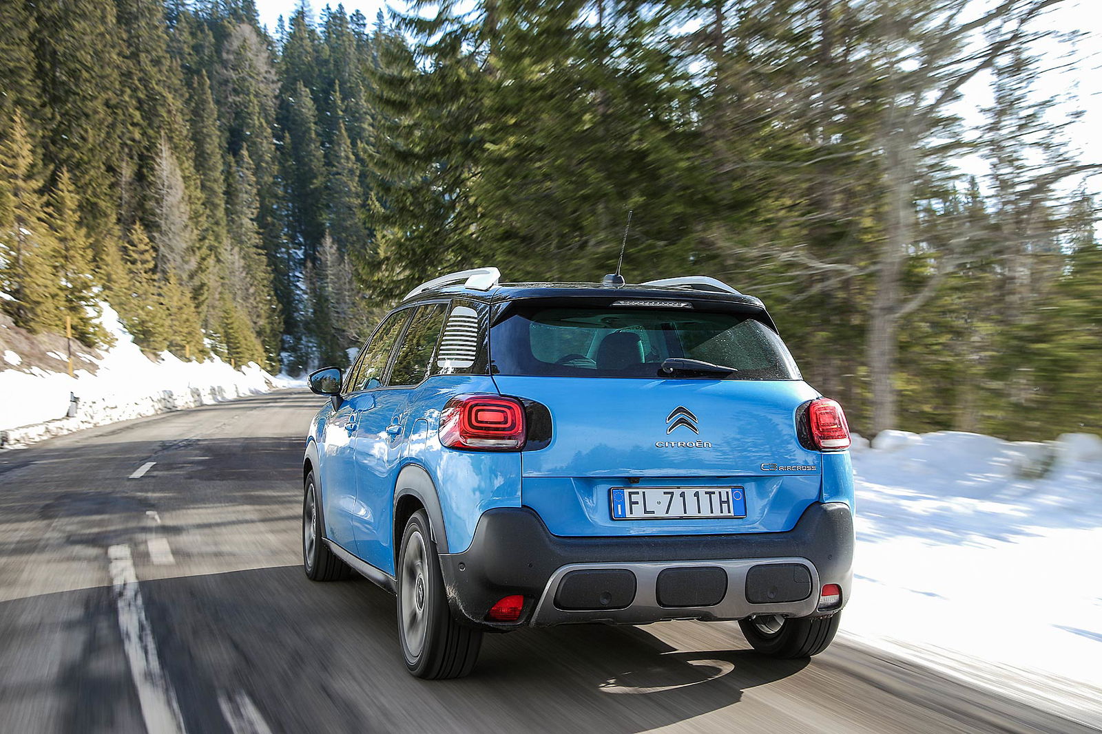 Citroën C3 Aircross azzurra vista posteriore su strada di montagna con neve e pini