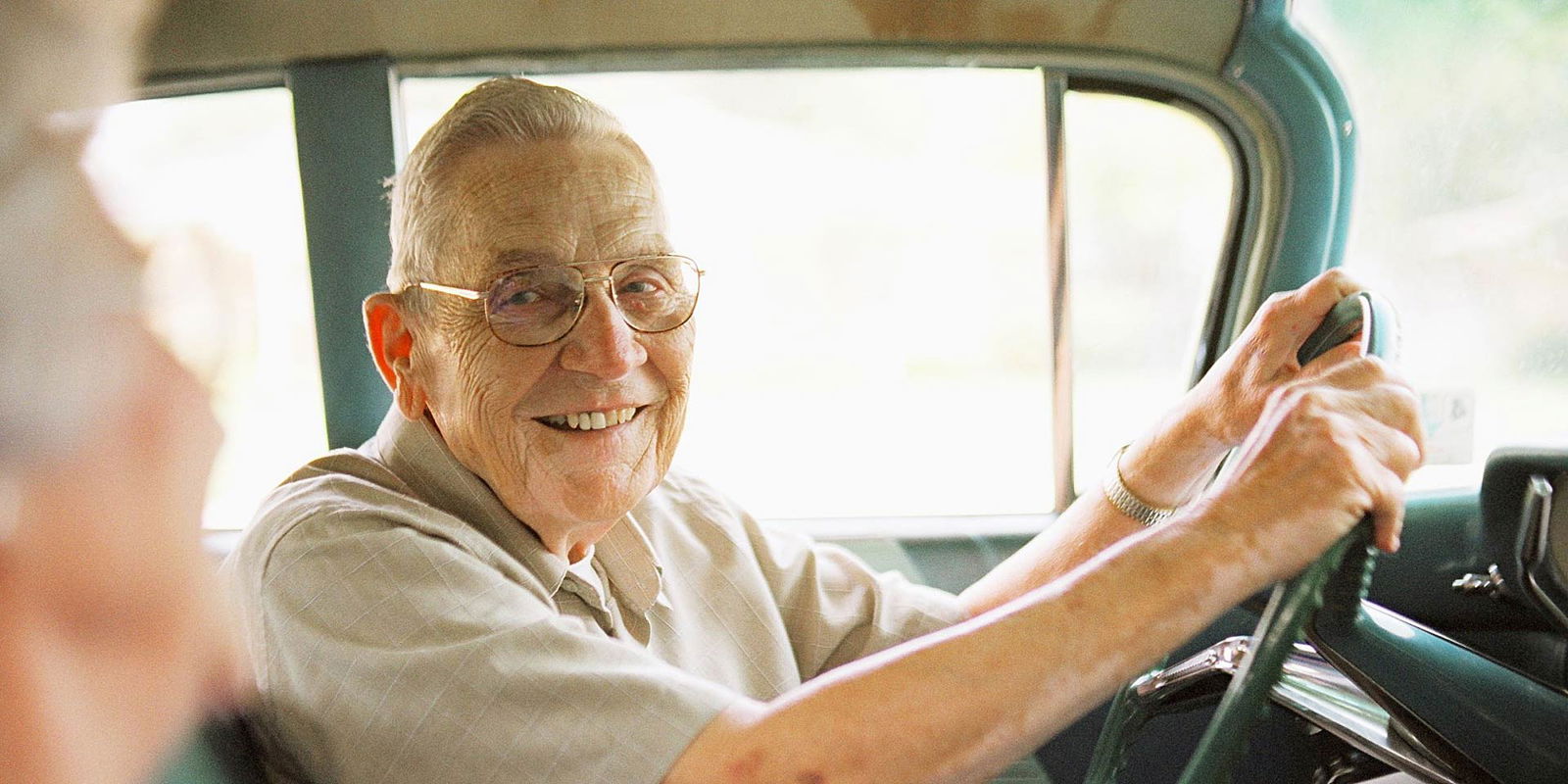 Anziano signore sorride alla moglie alla guida della sua auto
