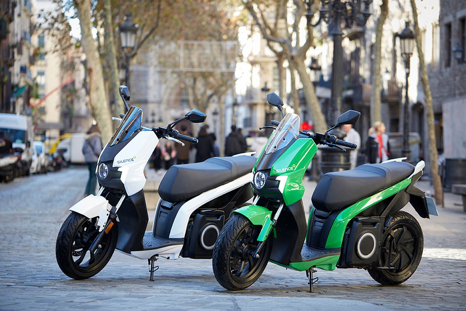 Scooter elettrico Silence S01, vista laterale statica in città, due modelli bianco e verde