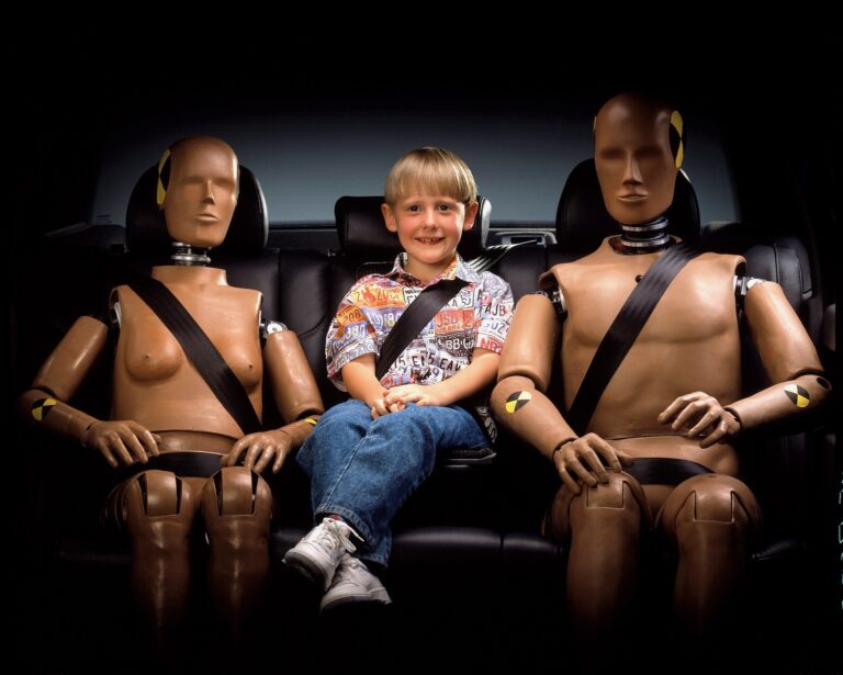 bambino seduto sul divano di una auto con due manichini da crash test