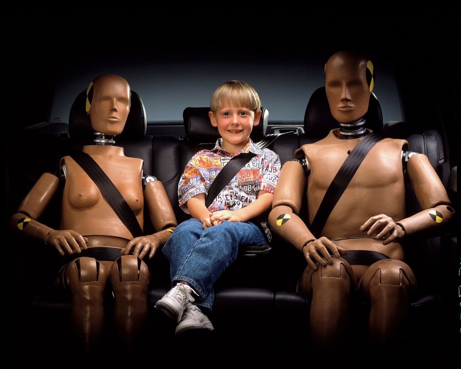 bambino seduto sul divano di una auto con due manichini da crash test